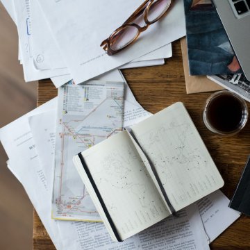a busy desk in the office filled with books, notes and a cup of coffee